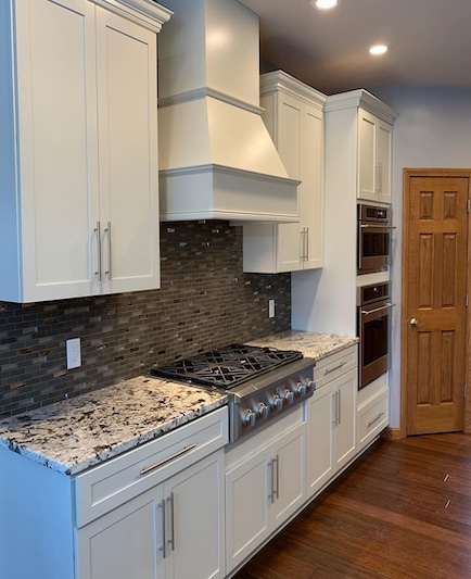 Kitchen with white cabinets, granite counters, gas stove, built-in ovens, mosaic backsplash.