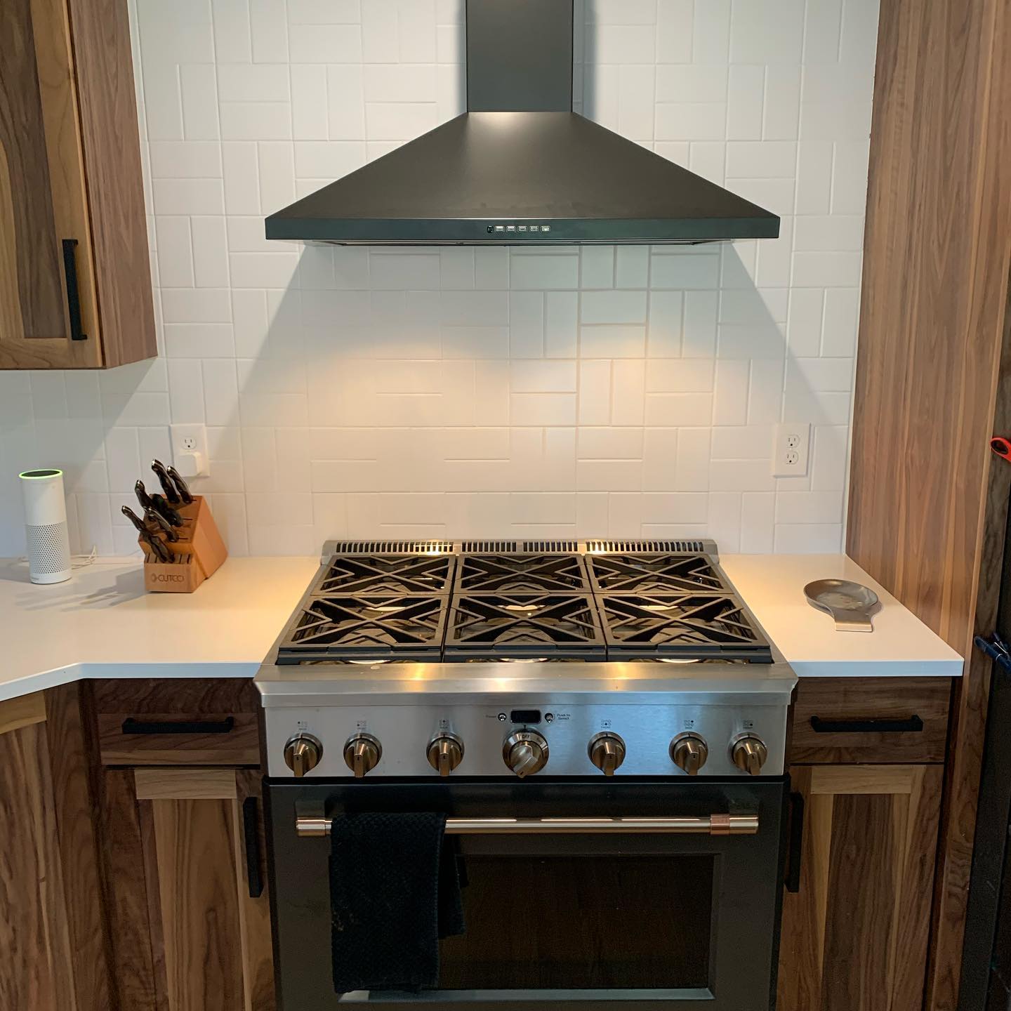 Chef's kitchen: six-burner stove, professional hood, white backsplash, and knife block.